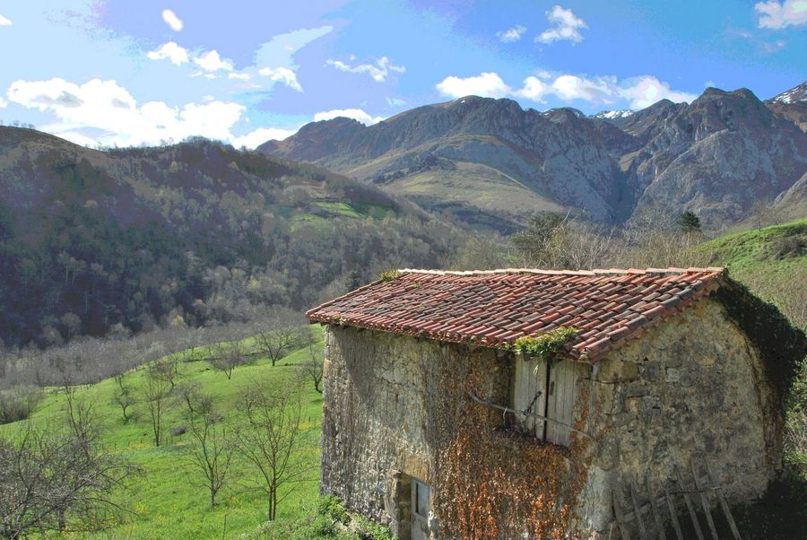 A stone building in green hill country below the mountains of Asturias