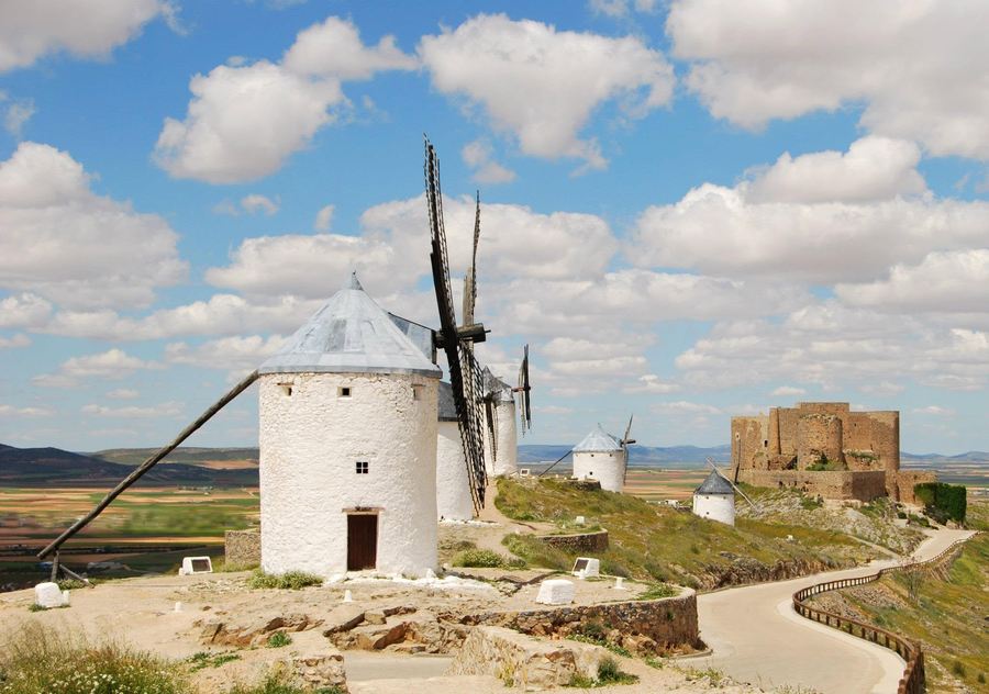 A line of whitewashed windmills along a ridge in Castilla-La Mancha with a castle beyond