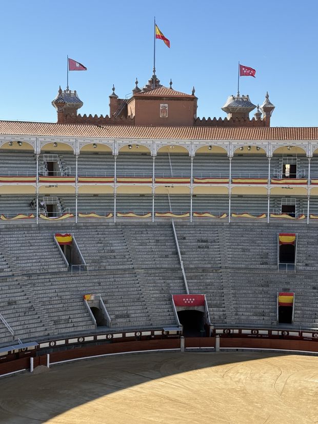 The interior of the Las Ventas bullring in Madrid, empty, with the tiled roofline and flags above the arcade